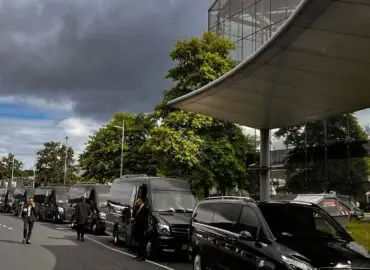 Luxuriöse Transferfahrzeuge vor einem belebten Messegelände.